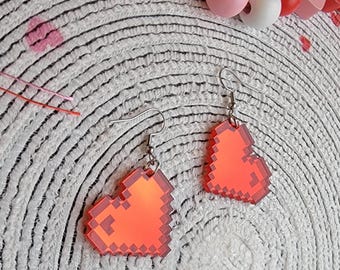 May include: A pair of red pixel heart earrings with silver hooks. The earrings are on a white background with a circular pattern.