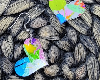 May include: A pair of heart-shaped earrings with a colorful abstract design. The earrings are made of clear resin with a silver hook.