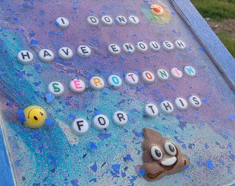 May include: A framed artwork with a blue border, featuring the phrase "I DON'T HAVE ENOUGH SEROTONIN FOR THIS" spelled out with white letter beads. Includes a yellow smiley face and a brown poop emoji.