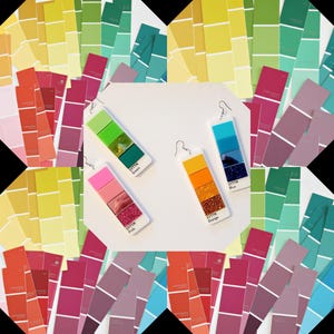 Op de afbeelding: Oorbellen met kleurverloopontwerpen in groen, roze, oranje en blauw. Elke oorbel heeft een rechthoekige vorm met een reeks kleurblokken en glitteraccenten. De oorbellen worden gepresenteerd tegen een achtergrond van kleurstalen.