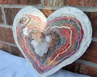 May include: A heart-shaped resin art piece with a white, red, and brown layered design. The resin is filled with glitter and a clear quartz crystal.