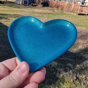 Op de afbeelding: Een teal hartvormige schaal met een glinsterende afwerking. De schaal is gemaakt van hars en is perfect voor het bewaren van kleine items zoals sieraden of sleutels.