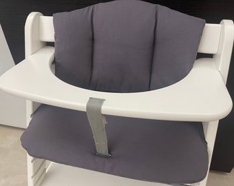 May include: White high chair with a gray padded seat and a white tray. The chair has a strap to secure a child in the seat.
