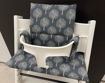 Puede incluir: Silla alta blanca con un cojín estampado en gris y blanco. El cojín tiene un patrón repetitivo de árboles blancos sobre un fondo gris oscuro.