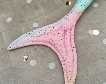 May include: A pink and blue mermaid tail with gold glitter. The tail is made of fabric and has a pointed fin.