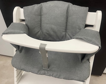 May include: A white high chair with a gray fabric seat and back cushions. The chair has a white tray with a gray strap.
