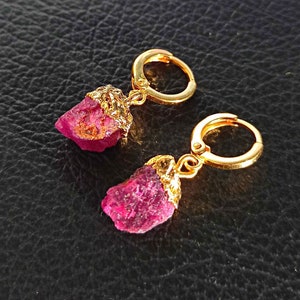 Può includere: Un paio di orecchini a cerchio dorati con un ciondolo di pietra preziosa rosa. La pietra preziosa ha una forma naturale e grezza.