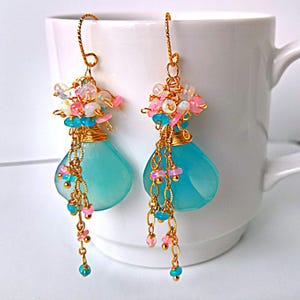 May include: Gold dangle earrings with turquoise blue teardrop shaped stones, pink and white beads, and gold chains.