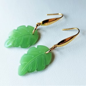 Könnte beinhalten: Ein Paar goldene Blatt-Ohrringe mit grünen Jade-Blatt-Anhängern. Die Blätter haben ein detailliertes Adernmuster.