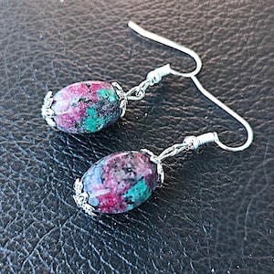May include: A pair of silver earrings with oval-shaped green and pink stones. The stones have a speckled pattern.
