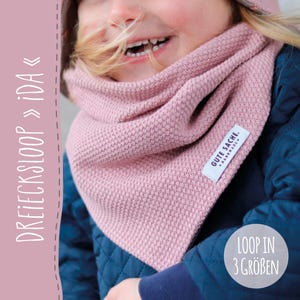 Könnte beinhalten: Ein rosa gestrickter Dreiecksschal mit einem "GUTE SACHE. HANDMADE." Etikett. Der Schal wird von einem Kind getragen und der Text "DREIECKSLOOP >> IDA" ist auf der linken Seite des Bildes sichtbar. Der Text "LOOP IN 3 GRÖßEN" ist auf der rechten Seite des Bildes sichtbar.