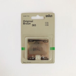 Puede incluir: Una pieza de repuesto para cabezal de afeitadora Braun de color plateado en un paquete de plástico transparente con fondo blanco. El paquete tiene el texto "Original Braun 383" y "Made in Germany".