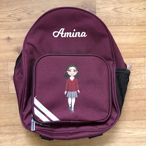 May include: Burgundy backpack with white stripes and a black mesh pocket. The backpack has a personalised name, "Amina", embroidered on the front. A cartoon girl in a school uniform is printed on the front of the backpack.