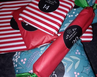 May include: Several gifts wrapped in red and white striped paper and teal paper with a holly pattern. A red paper-wrapped cylinder tied with green ribbon features a black circular label with the text Familiars Witchcraft and the number 20.