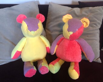 May include: Two colorful patchwork teddy bears with purple, yellow, pink, and green fabric. The bears are sitting on a gray couch.