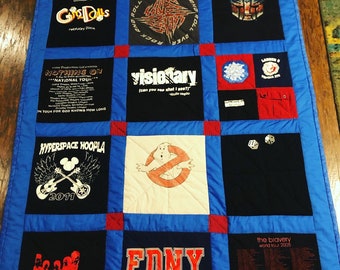 May include: A blue and red patchwork quilt made from t-shirts. The quilt features various band logos and designs, including "Gods & Dolls", "Nothing On", "Visionary", "Hyperspace Hoopla", "FDNY Ladder 8", and "The Bravery".