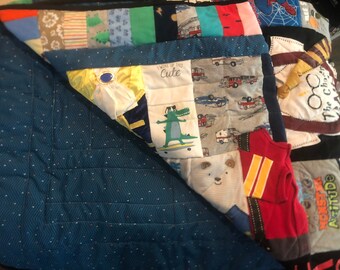 May include: A blue and white patchwork quilt with a variety of designs, including a fire truck, a crocodile, and a Harry Potter themed patch. The quilt is made from a variety of fabrics, including cotton and flannel. The quilt is folded in half and the back side is a solid blue color with white polka dots.
