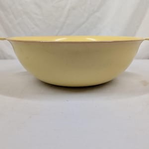 May include: A pale yellow mixing bowl with a smooth, rounded interior and exterior. The bowl features a wide, open top with a slightly flared rim and two small, integrated tab handles on opposite sides, providing a simple, functional design.