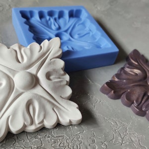 May include: Two white and purple decorative moldings with a floral design, and a blue silicone mold for making the moldings.