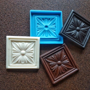 Può includere: Quattro piastrelle quadrate con un motivo floreale in rilievo. Le piastrelle sono di diversi colori: blu, bianco, nero e marrone.