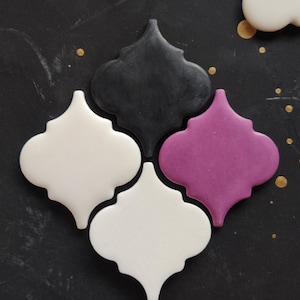 May include: Four ceramic tiles in the shape of a quatrefoil. The tiles are in black, white, and purple.