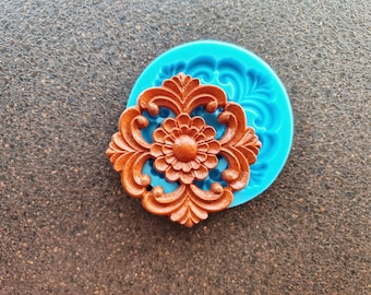 May include: A silicone mold for making resin crafts. The mold is blue and features a detailed floral design. The mold is shown with a brown resin casting of the design.