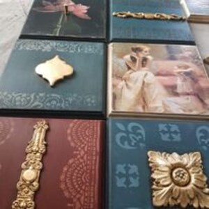 K&ouml;nnte beinhalten: Ein Set aus sechs dekorativen Wandfliesen mit verschiedenen Designs. Die Fliesen zeigen ein Blumenmuster, einen goldenen Metallakzent, eine Frau in einem Kleid, einen goldenen Metallakzent, einen goldenen Metallakzent und ein geometrisches Muster. Die Fliesen sind in Blaut&ouml;nen, Gr&uuml;n- und Goldt&ouml;nen bemalt.