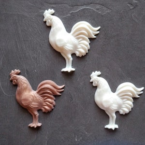 May include: Three rooster figurines, one white, one brown, and one off-white, with detailed features and a textured finish.