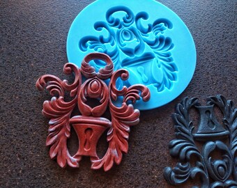 May include: Two ornate, decorative molds for making resin crafts. One mold is blue silicone and the other is a red resin casting of the design. The design is a stylized, ornate keyhole.