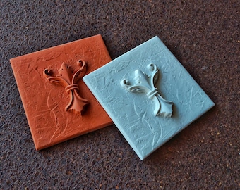 May include: Two square wall decor pieces with a raised, ornate design in the center. One is painted a rusty orange color and the other is painted a light blue color.