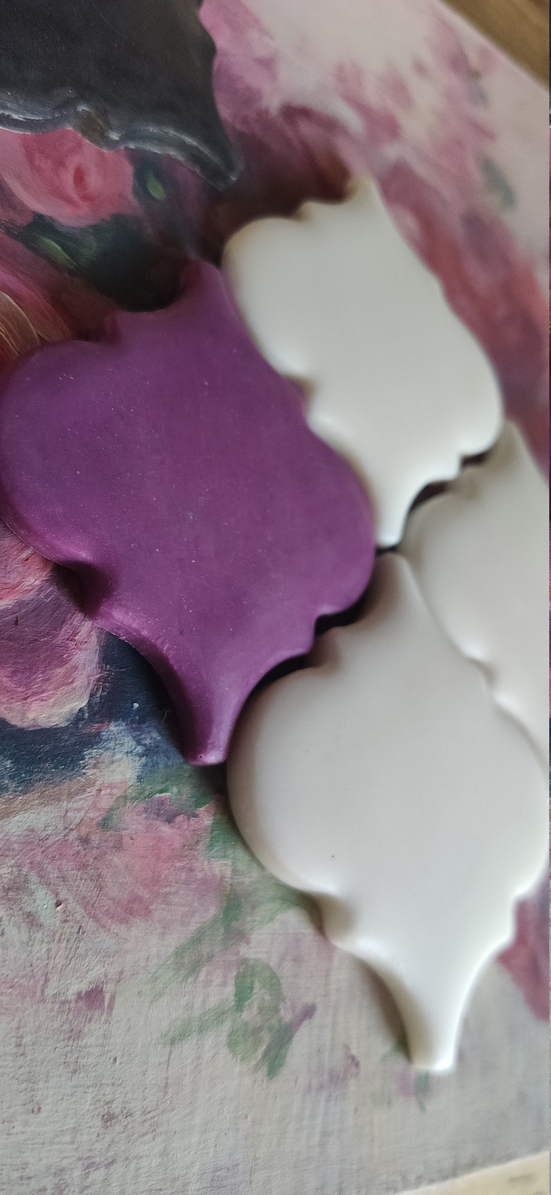 May include: Two ceramic tiles in the shape of a quatrefoil. One tile is purple and the other is white.