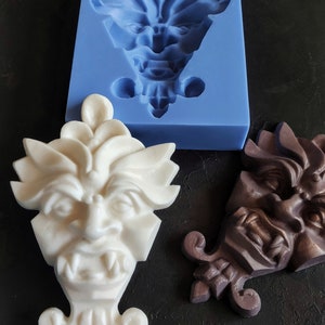 May include: Two white and brown resin gargoyle sculptures with detailed faces and wings. The sculptures are on a black surface. One sculpture is in a blue silicone mold.