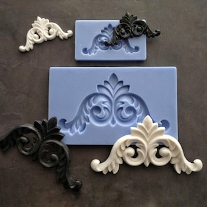 May include: Two silicone molds for making decorative cake or cookie accents. One mold is larger and features a single, ornate, symmetrical design. The smaller mold features two smaller, symmetrical designs.
