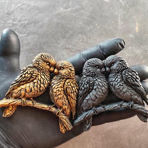 May include: A decorative sculpture featuring four detailed owl figurines perched on a branch. Two owls are gold-toned, and two are silver-toned. The owls are arranged in pairs, with each pair touching beaks.