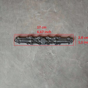 K&ouml;nnte beinhalten: Ein silberfarbener T&uuml;rgriff aus Metall mit filigranen Details. Er ist 17 cm lang und 2,8 cm breit.