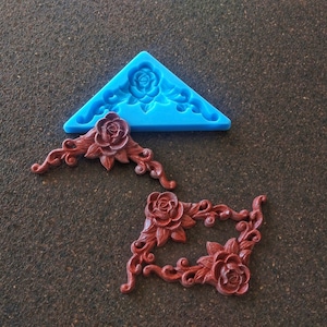 May include: Two silicone moulds for making decorative corner pieces. One mould is blue and the other is brown. Both moulds feature a rose design.