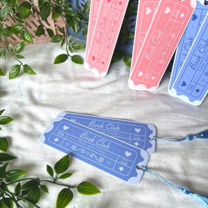 May include: Two blue and two pink bookmarks with a ticket design. The bookmarks have the text "Book Club" and "Once upon a time" on them. The bookmarks have a star, hearts, and a swirl design.