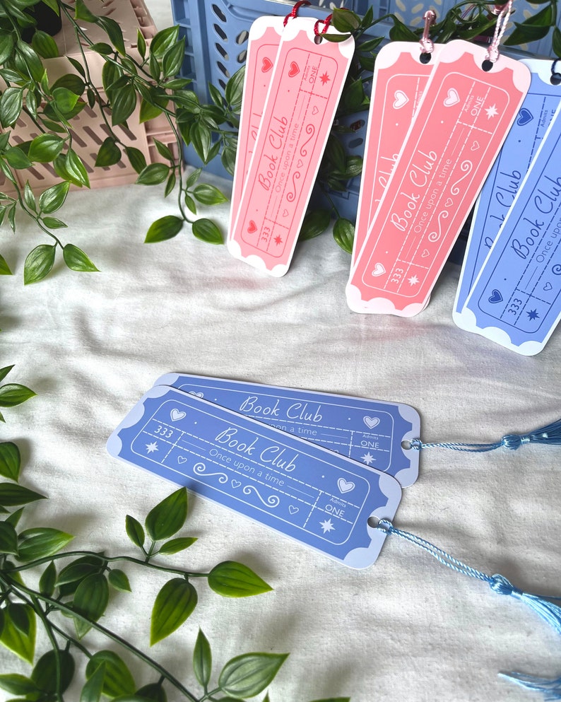May include: Two blue and two pink bookmarks with a ticket design. The bookmarks have the text "Book Club" and "Once upon a time" on them. The bookmarks have a star, hearts, and a swirl design.