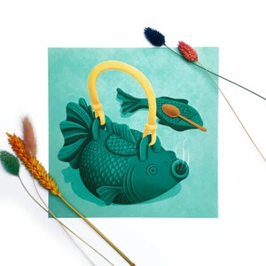 Può includere: Una teiera blu turchese a forma di pesce con un manico e un beccuccio gialli. La teiera è appoggiata su uno sfondo blu turchese con un piatto più piccolo a forma di pesce e un cucchiaio di legno.