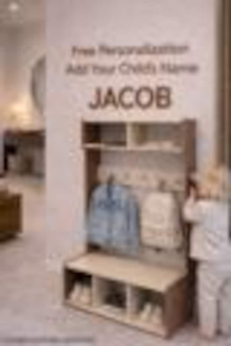 May include: A light brown wooden entryway storage unit featuring an upper shelf, a middle section with hooks for hanging items, and a bottom bench with three open cubbies for shoe storage. The text "Free Personalization Add Your Child's Name JACOB" is visible.