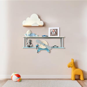 May include: A blue and white airplane-shaped shelf with a propeller, two shelves, and a cloud-shaped shelf above it. The shelf is decorated with stuffed animals, toy cars, and a framed photo.