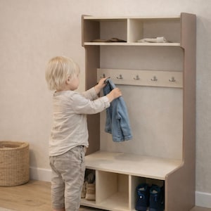 May include: A light-colored wooden storage unit featuring an upper shelf with two compartments, a middle section with five silver metal hooks, and a lower bench area with three open cubbies for shoe storage. The unit has a smooth, light wood finish.