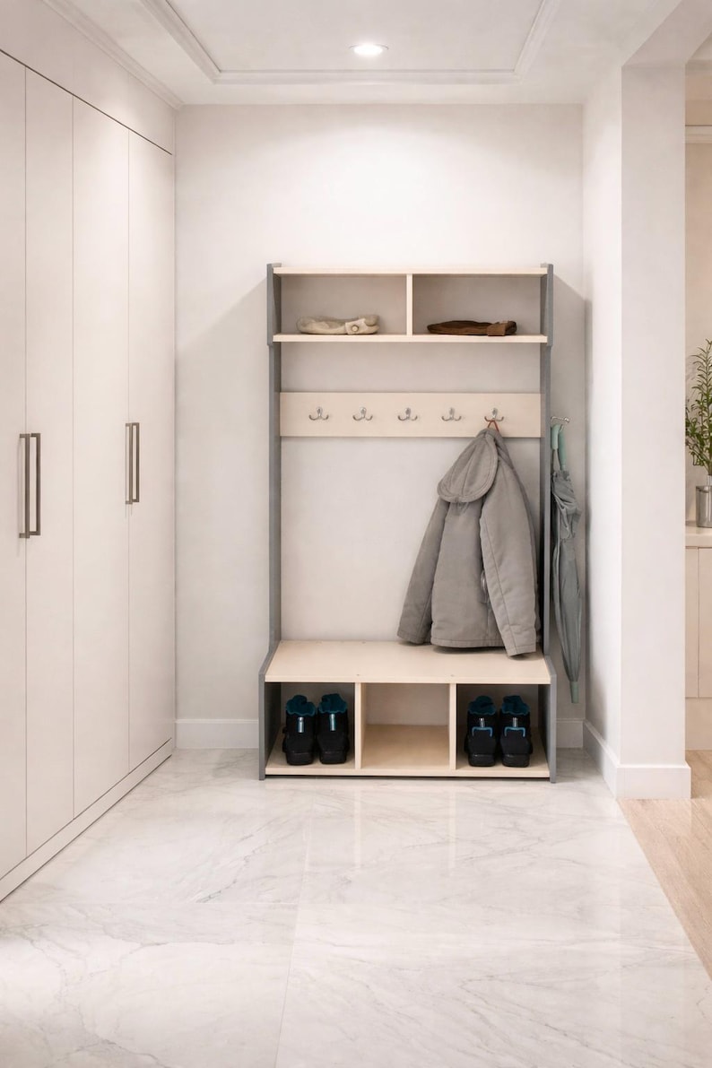 May include: A light wood and grey hall tree featuring an upper shelf with two compartments, a middle section with five metal hooks for hanging items, and a lower bench with three open storage cubbies for shoes, positioned against a white wall.