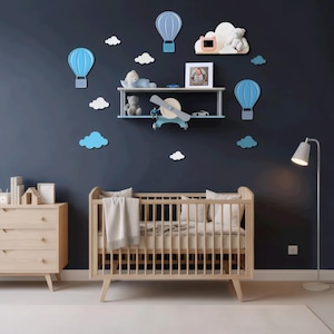 Pode incluir: Um quarto de criança com um berço de madeira clara, uma cômoda e um candeeiro de pé. A parede azul marinho é decorada com balões de ar quente azuis e nuvens brancas. Uma prateleira exibe brinquedos e uma foto emoldurada, criando uma atmosfera lúdica.