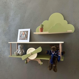 May include: Two wooden shelves in the shape of a cloud and an airplane. The cloud shelf is painted green and the airplane shelf is painted green and white. The airplane shelf has a propeller and wheels. There are stuffed animals on the shelves.