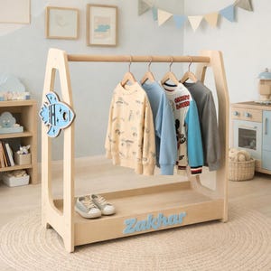 May include: A wooden children's clothing rack with a rocket ship design. The rack holds several sweaters and a pair of sneakers. The name "Zakhar" is displayed in blue letters on the front of the rack.