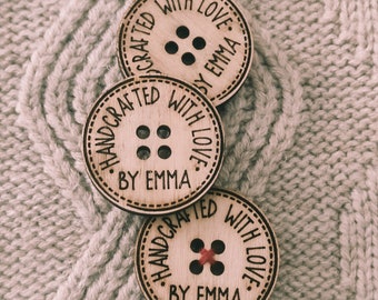May include: Three wooden buttons with the text "Handcrafted with love. By Emma."  The buttons have a brown wood grain and are decorated with a red thread.
