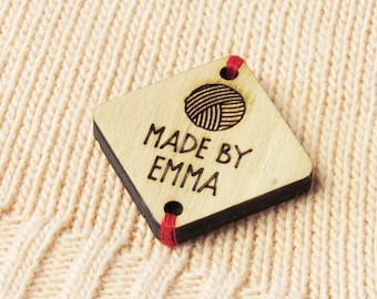 May include: A wooden tag with a yarn ball design and the text "MADE BY EMMA". The tag has red string attached to it.