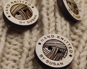 May include: Close-up of three wooden buttons with the text "HAND KNITTED BY SUSAN" engraved on them. The buttons are on a beige knitted fabric.
