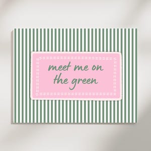 Peut inclure: Une carte rectangulaire avec un fond à rayures vertes et blanches. Un rectangle rose avec une bordure cousue blanche est centré, avec les mots "meet me on the green" en script vert.